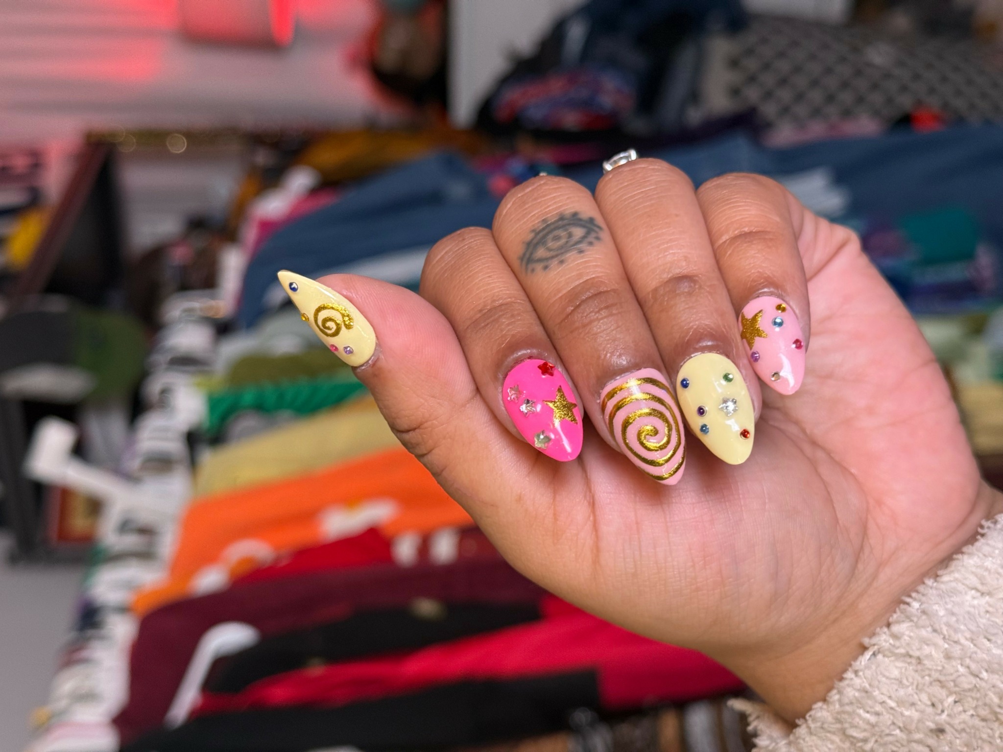 Hand with decorated nails, background of colorful fabric or clothing, fingers with various nail art designs.