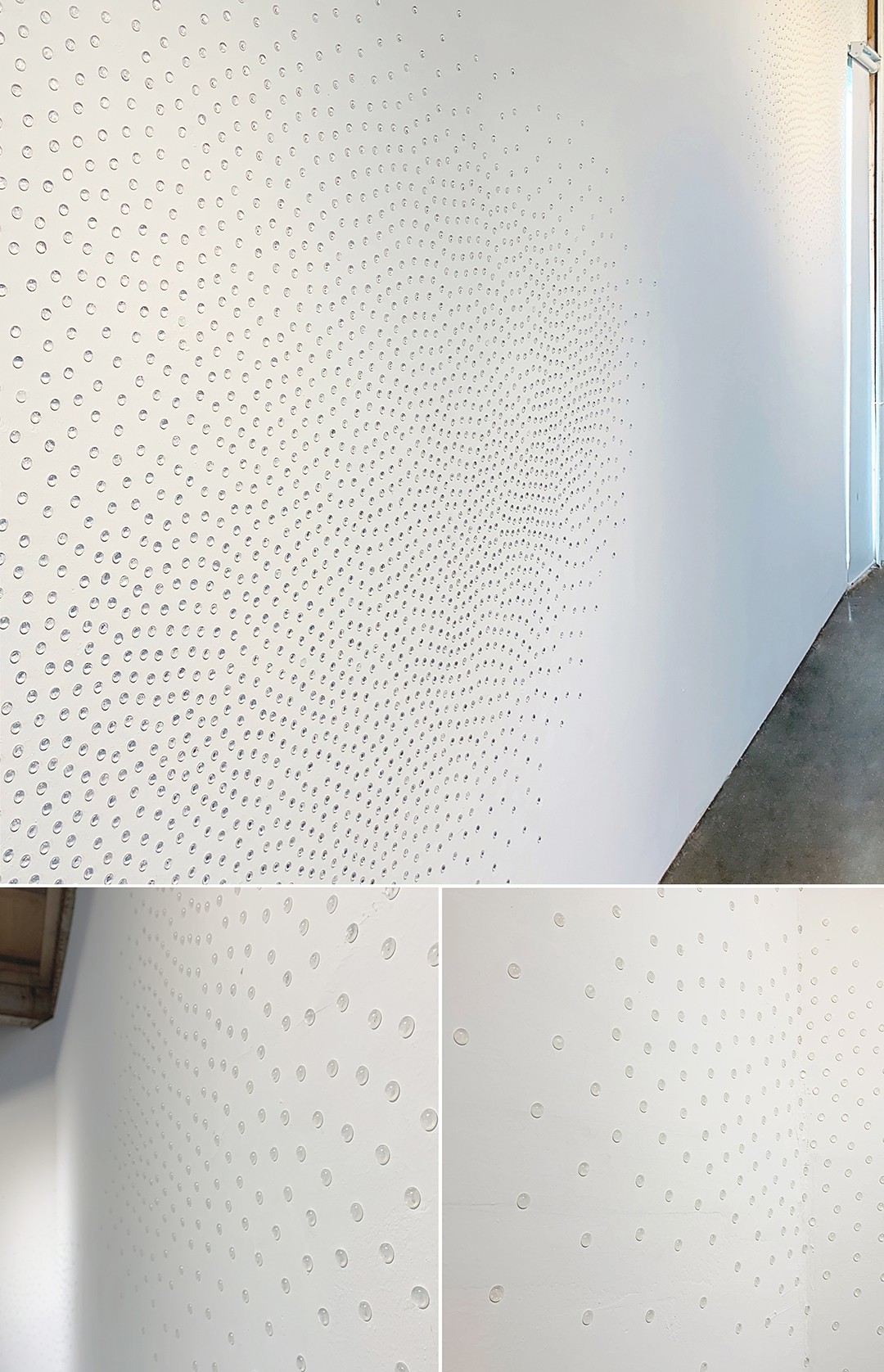 White wall with small circular perforations, corner of a room with a window, light coming in, and a dark floor.