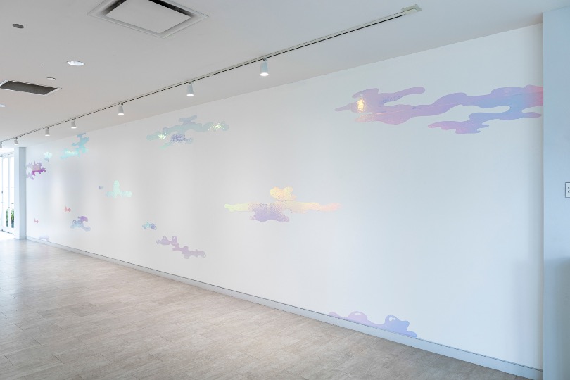 White wall with pastel-colored cloud illustrations, empty space, and a light-colored floor, in a modern interior setting.