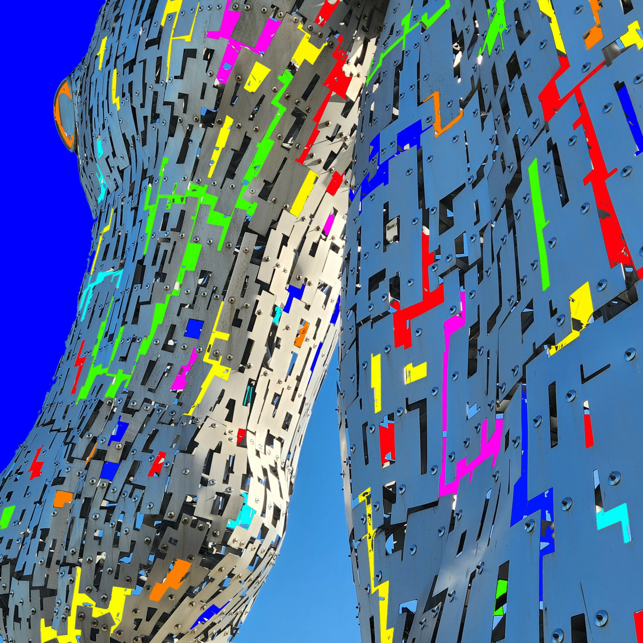 Close-up of a colorful, abstract, three-dimensional structure with various geometric shapes against a blue sky.