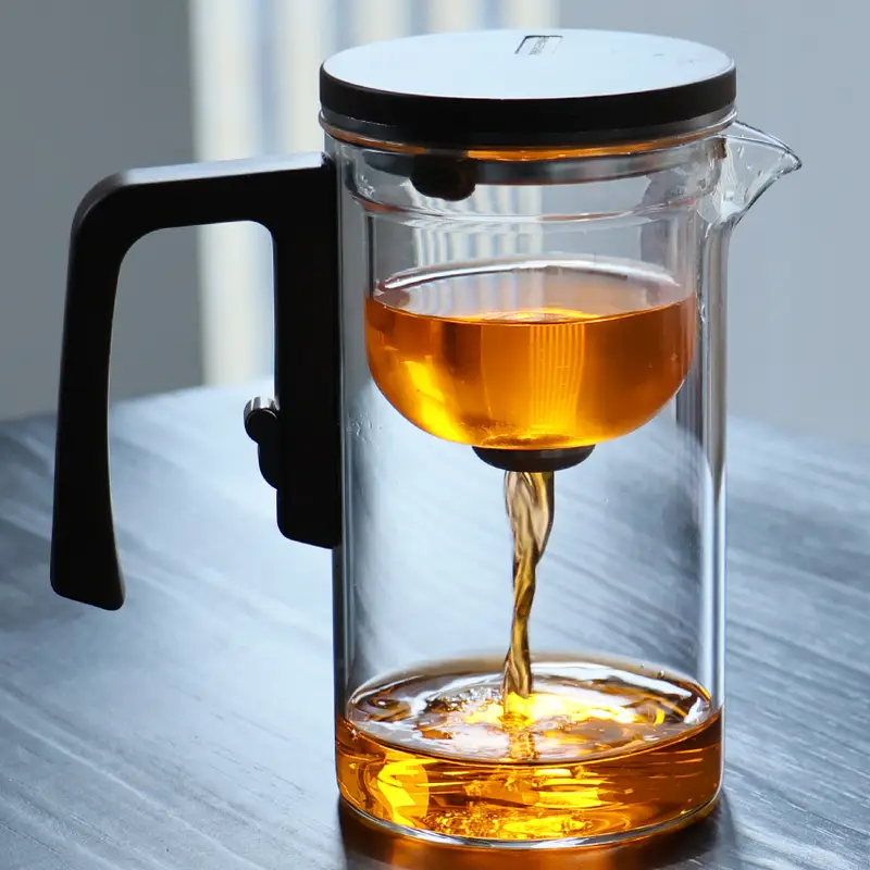 A glass teapot with a black handle and lid, filled with amber-colored tea, placed on a wooden surface.