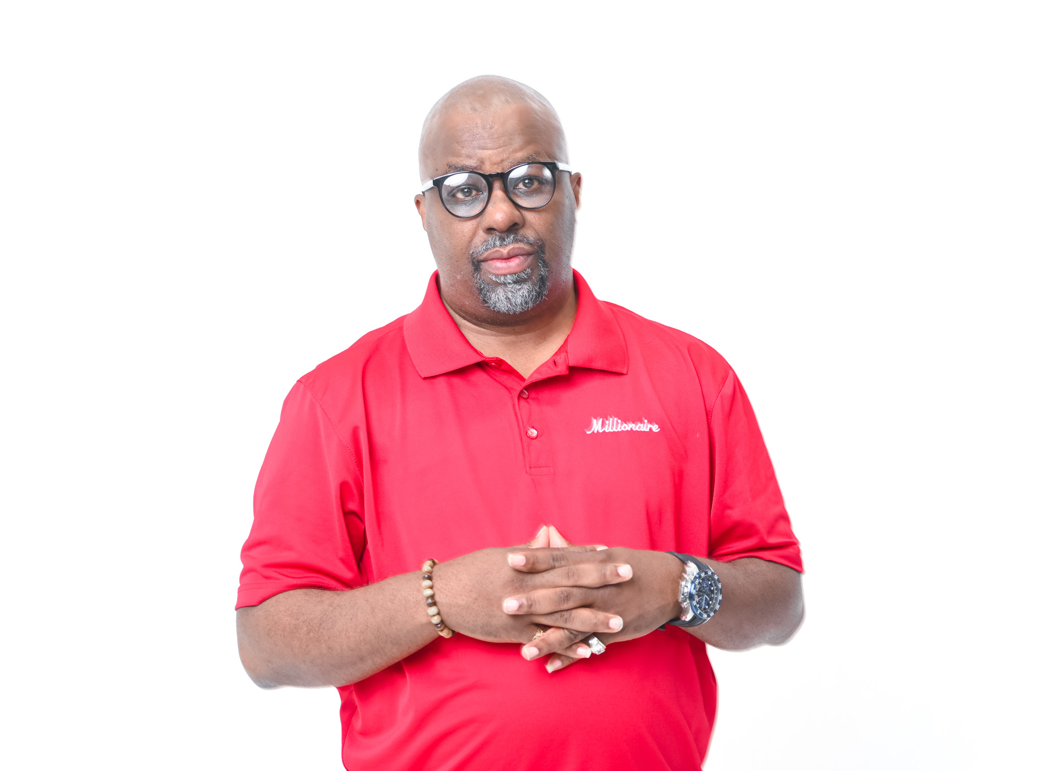 Man with glasses and a beard wearing a red polo shirt, standing with hands clasped, against a white background.