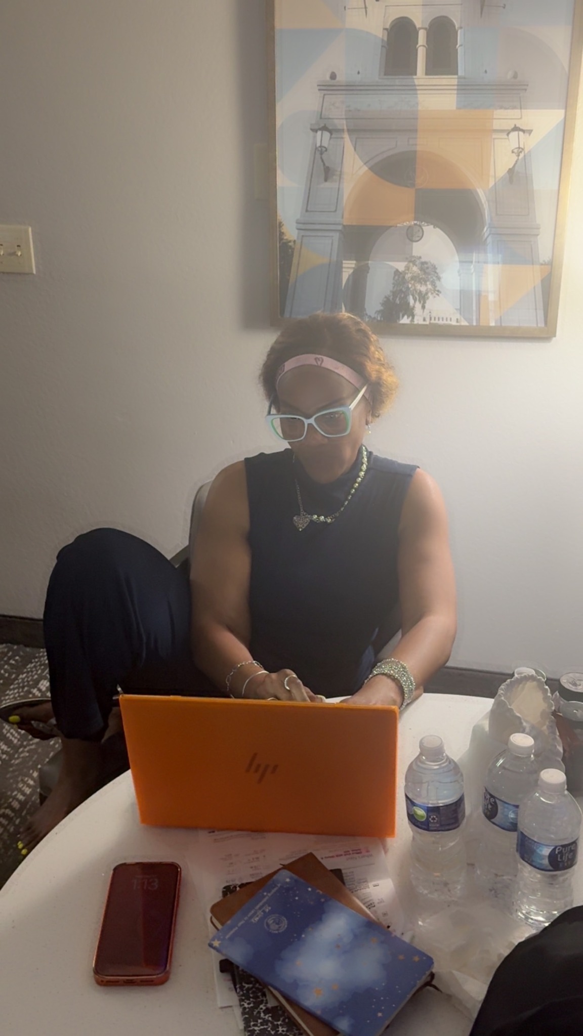 Person sitting at a table with a laptop, wearing glasses and a mask, with water bottles nearby.