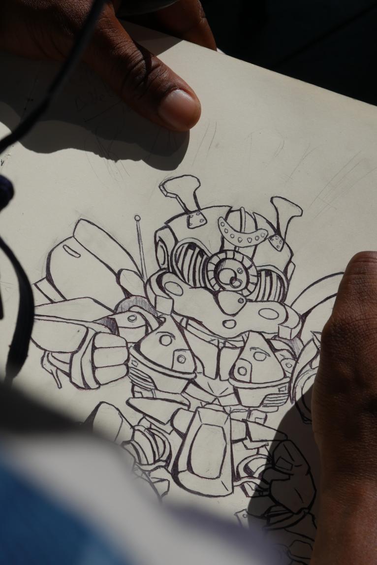 Person drawing a detailed robot with various mechanical parts on paper, hand visible holding a pen, shadow cast on paper