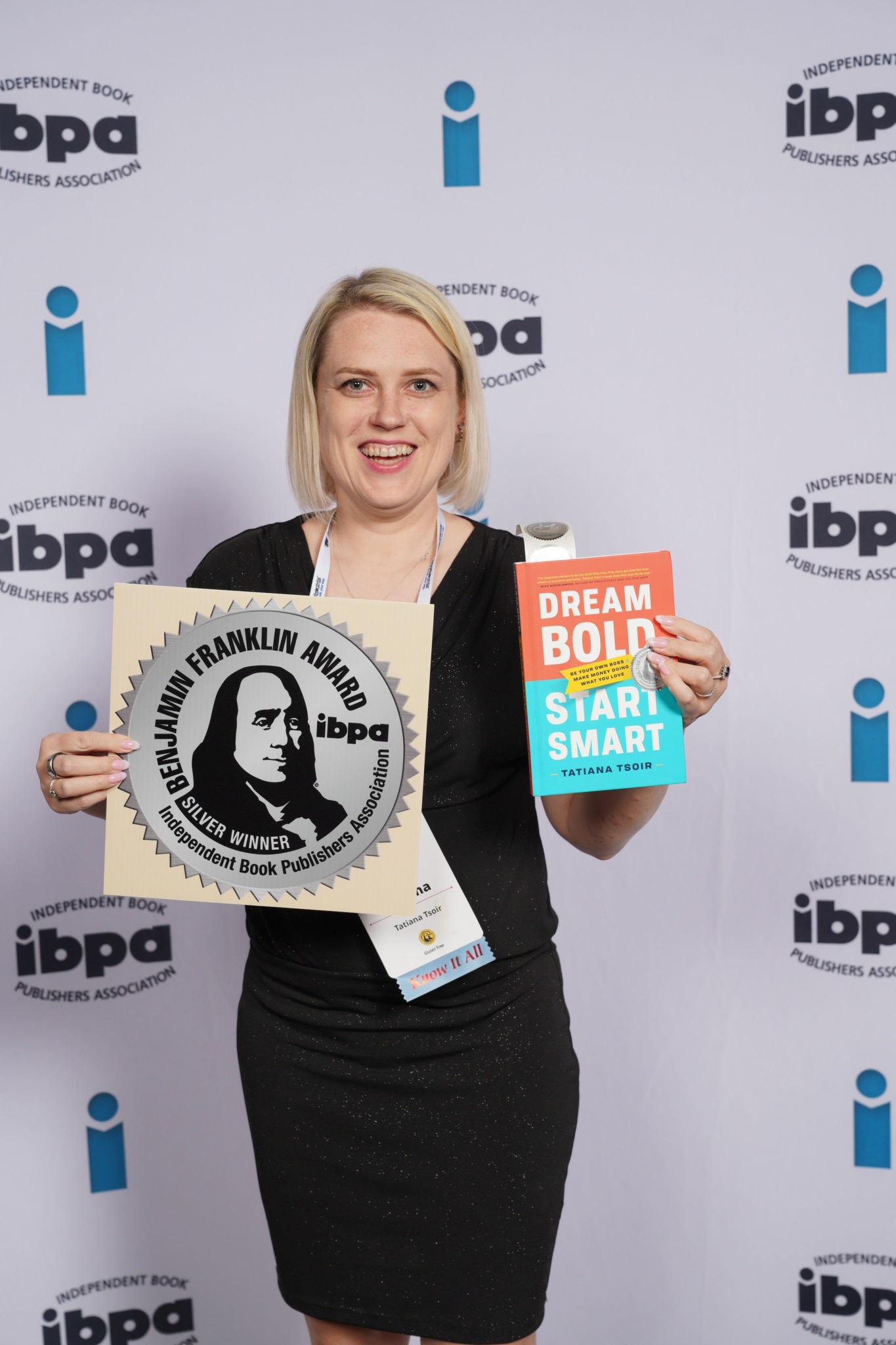 Woman holding a Benjamin Franklin award and a book titled 'Break the Body' at an event backdrop.