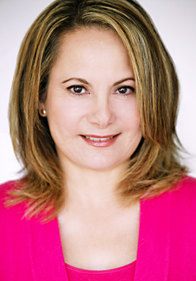 Portrait of a woman with shoulder-length hair wearing a pink top, smiling, against a plain background.