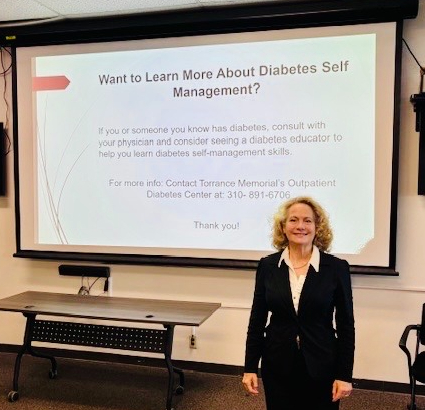 Woman in black blazer standing in front of a presentation screen with text about diabetes self-management.
