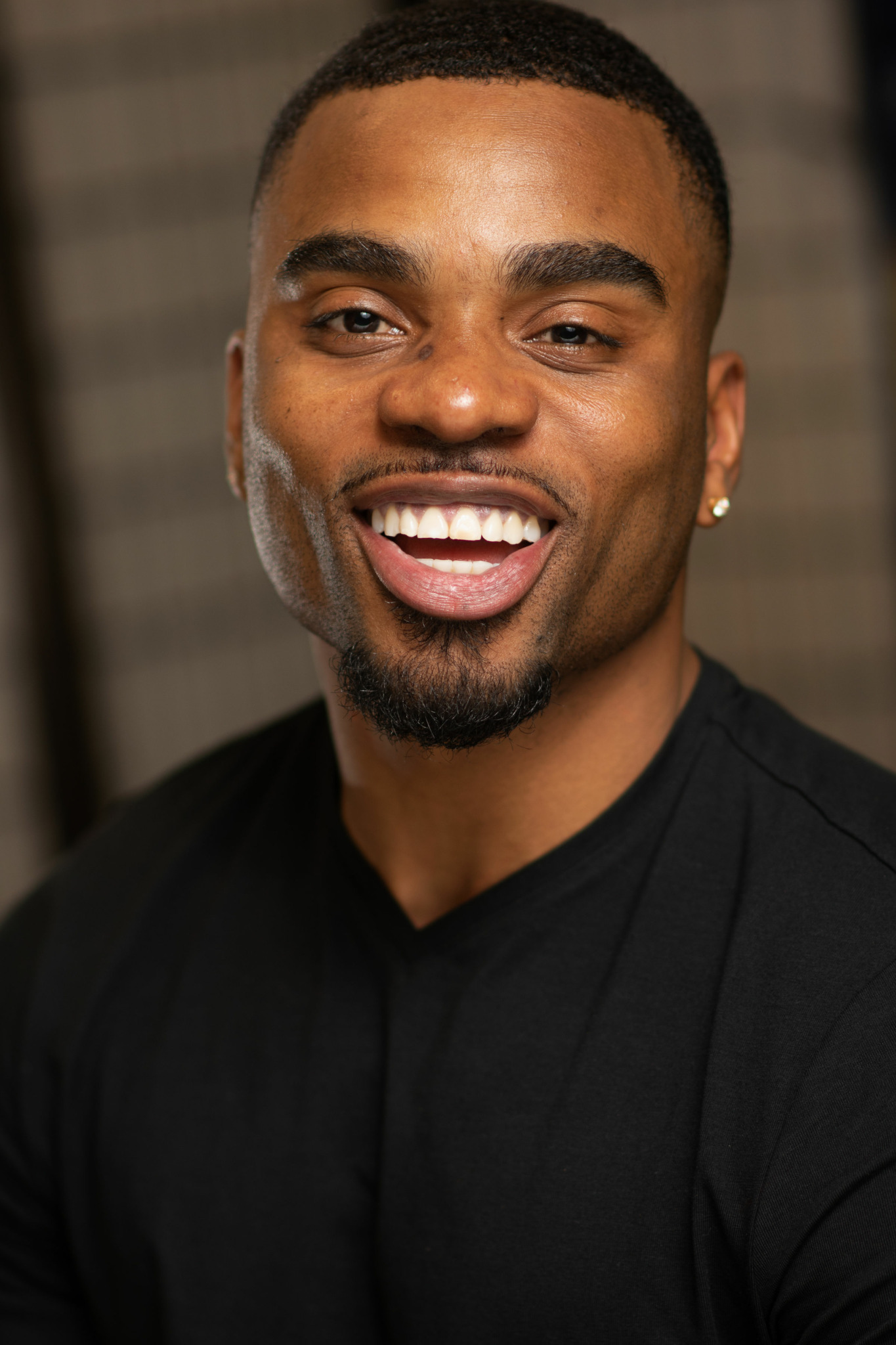 Smiling man with short hair, beard, and earrings, wearing a black shirt, in an indoor setting.