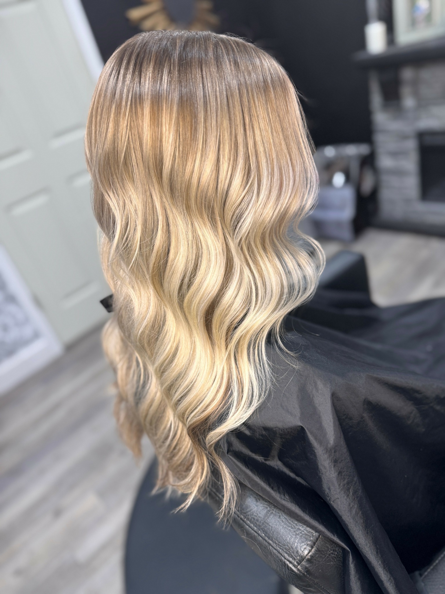 Back view of a person with long, wavy, blonde hair in a salon chair.