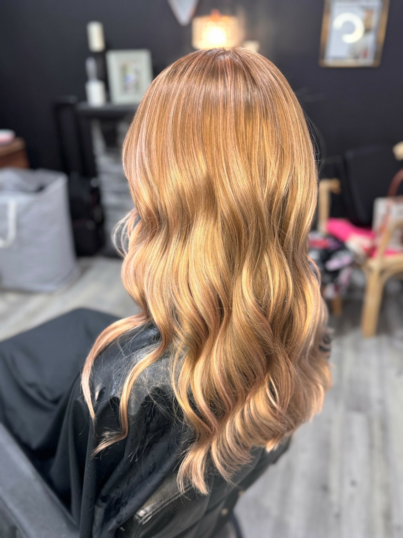 Back view of a person with long, wavy, blonde hair in a salon setting.
