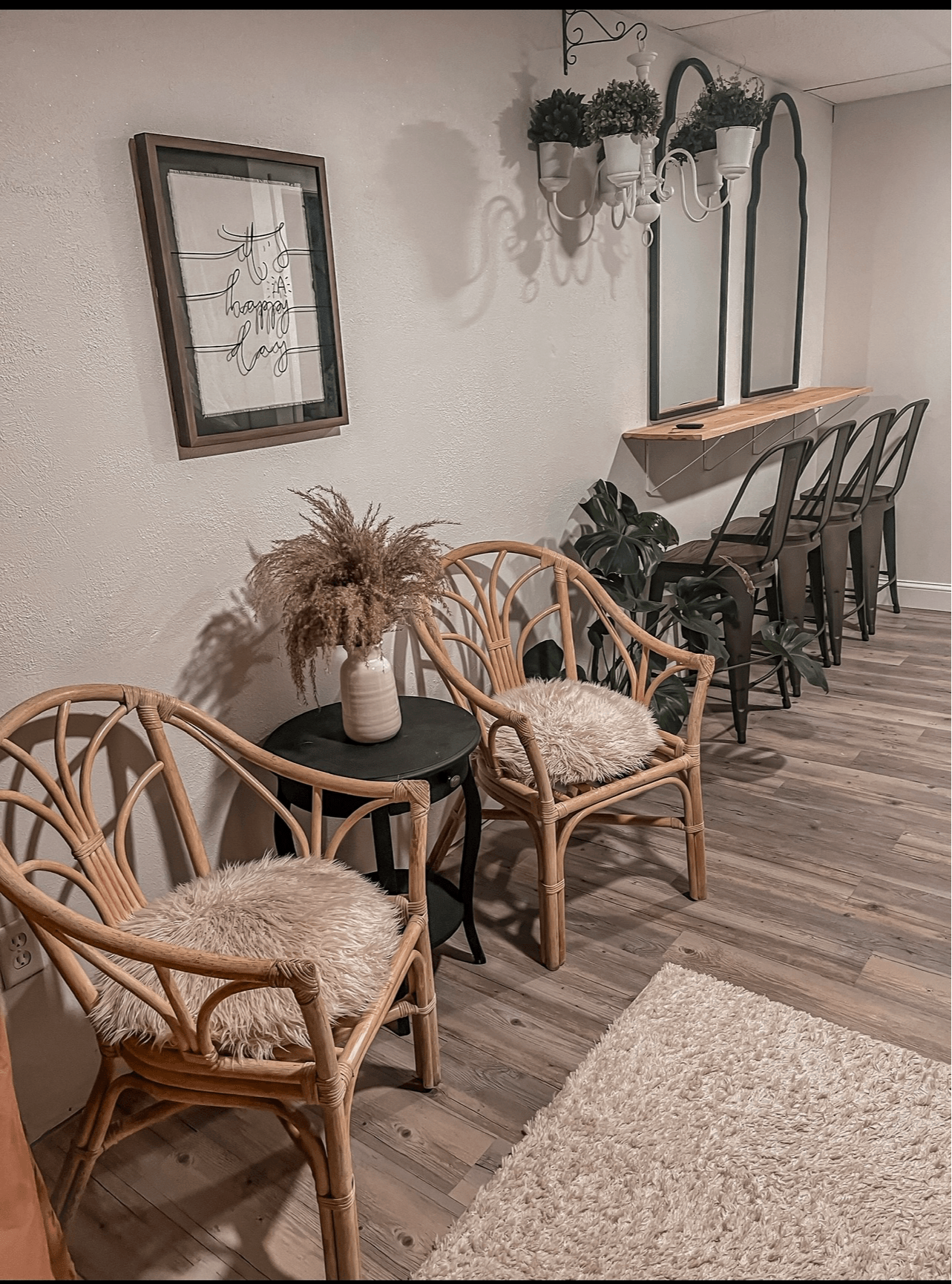 Living room corner with two rattan chairs, a small black table, a framed picture, and a wooden bar with chairs, hardwood floor.