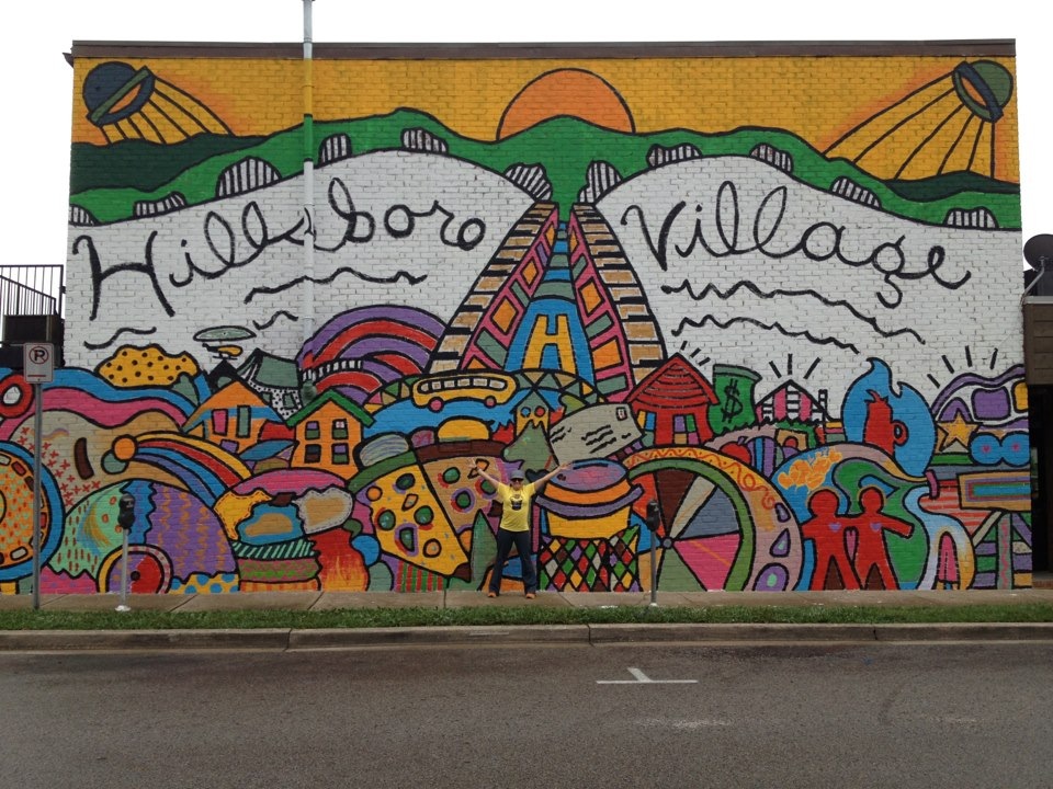 Colorful mural with houses, hills, and a sunset, featuring the words 'Hillsboro Village' in stylized script.