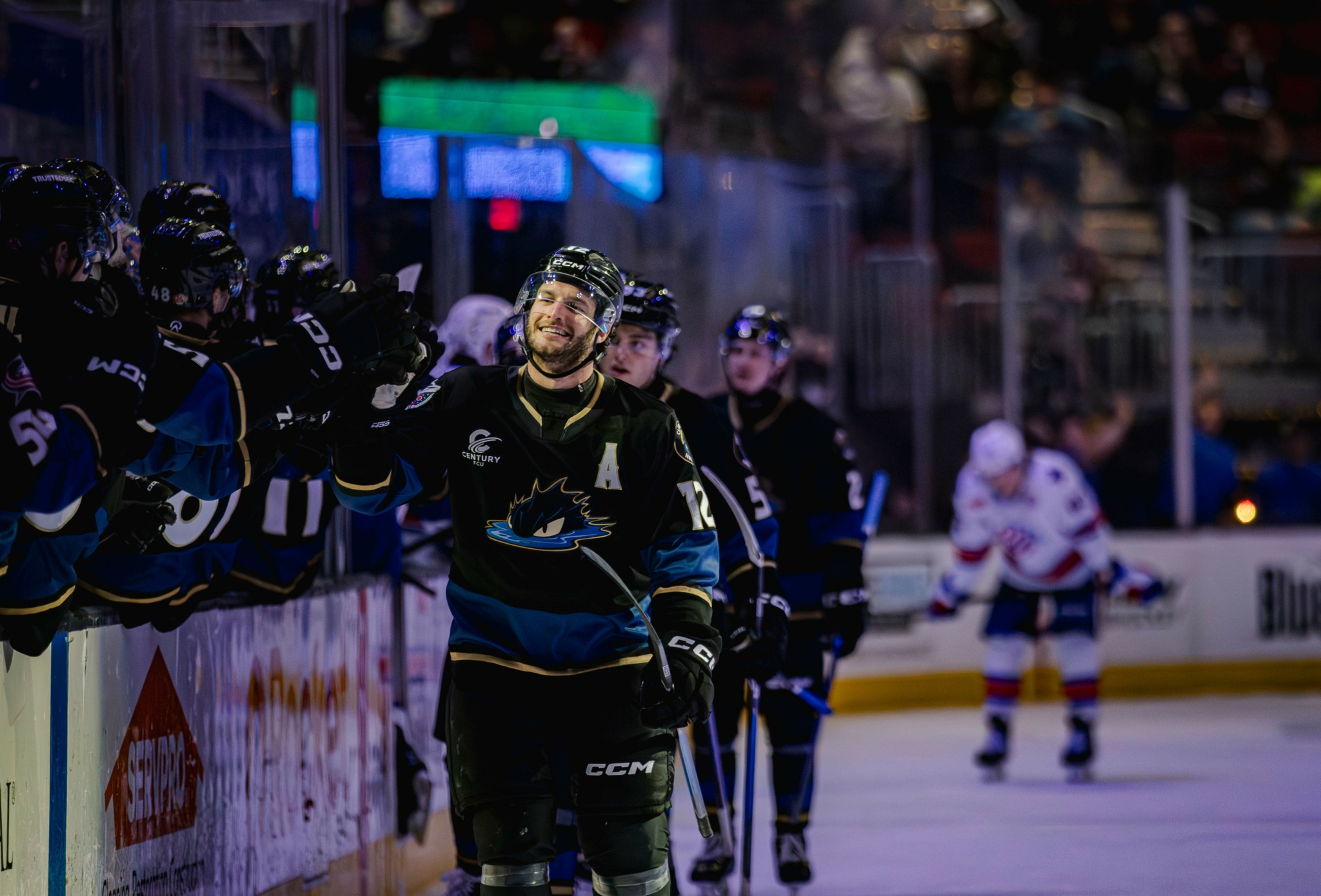 Hockey player standing on the ice rink with teammates and opponents in the background.