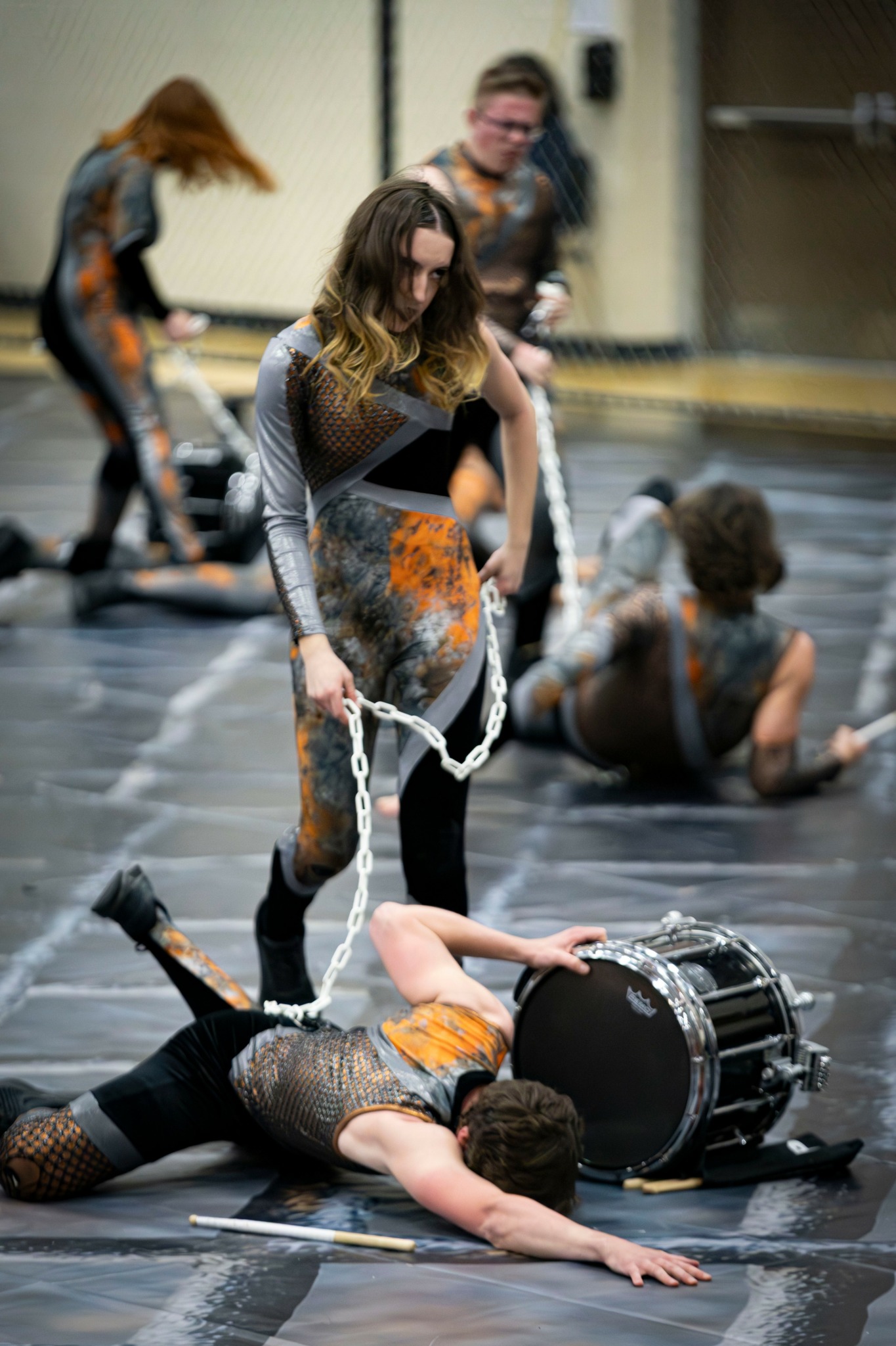 Group of performers on stage, some lying down, one holding a drum, in a dance or theatrical rehearsal.
