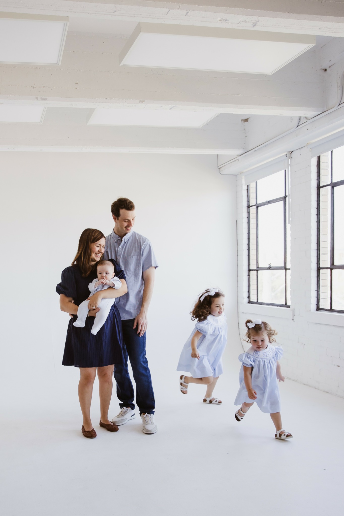 Family of four with two young children in a bright, spacious room with large windows and white walls.