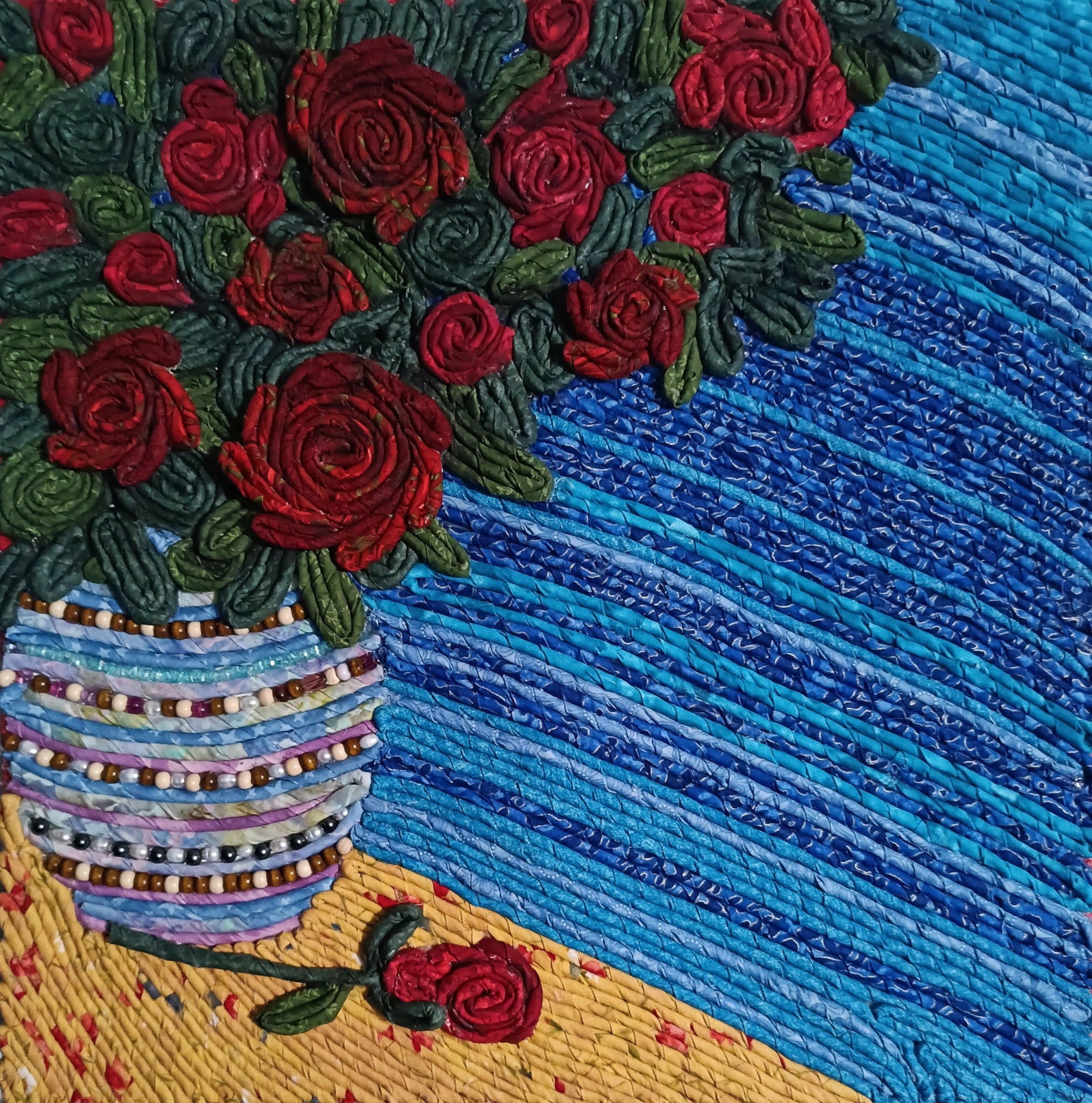 A bouquet of red roses in a striped vase on a yellow surface with a blue textured background.