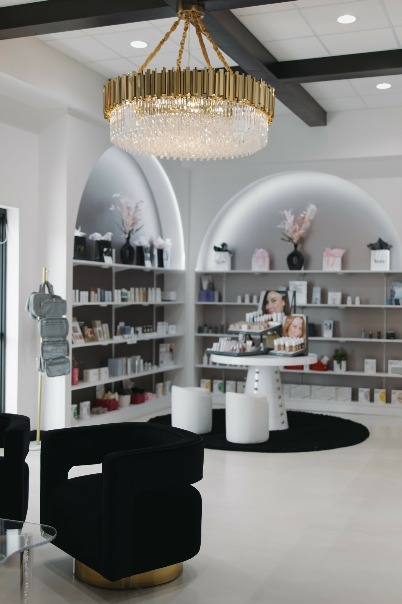 Modern interior with a large chandelier, black seating, and shelves with decorative items and books, in a bright space.