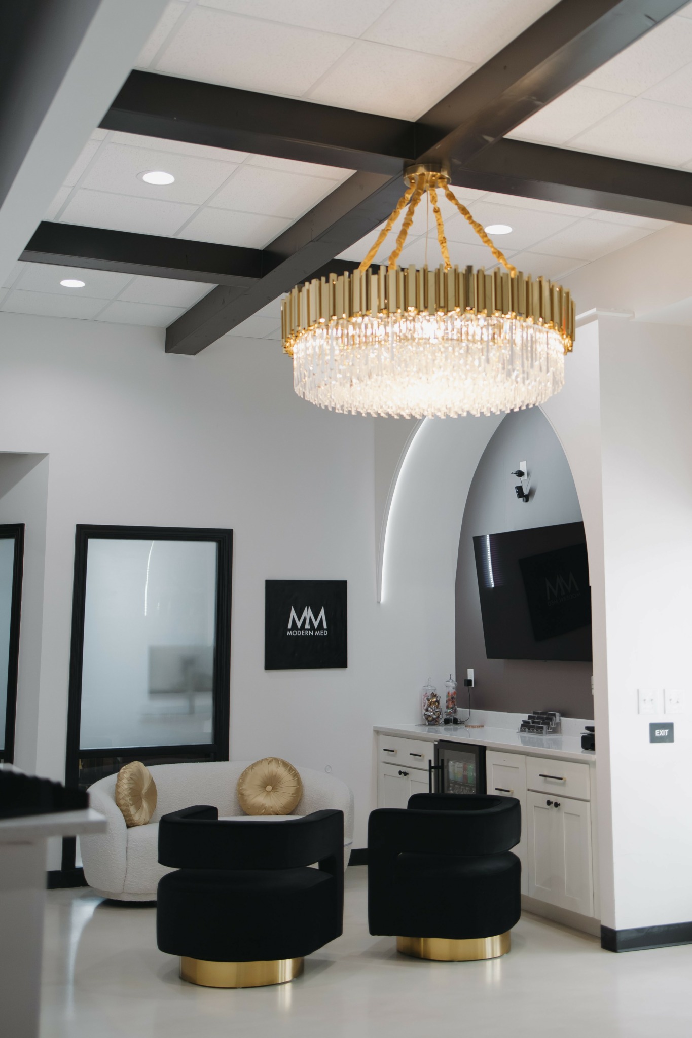 Elegant chandelier with gold and crystal elements hanging from a ceiling with dark beams, in a modern living room.