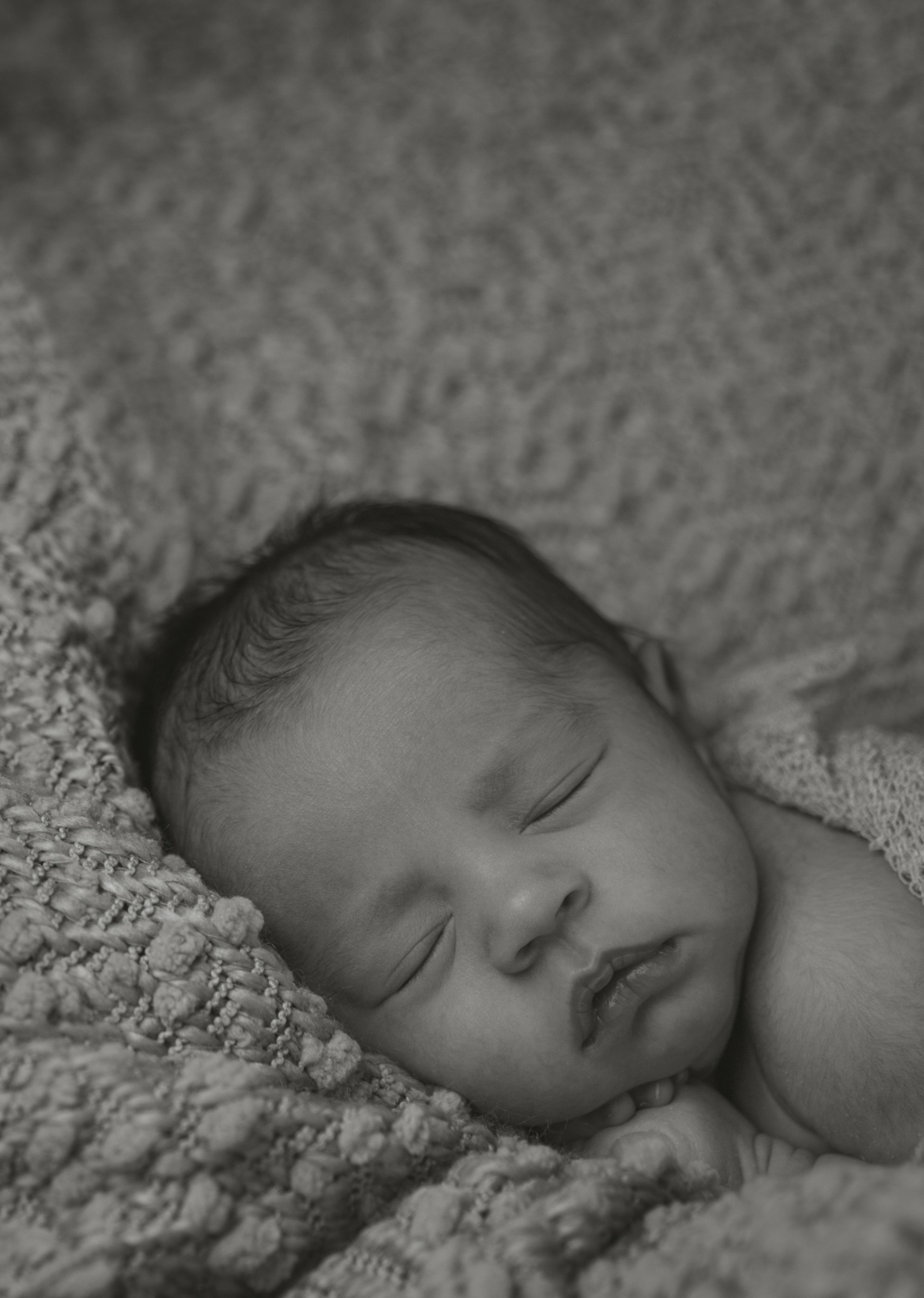 A sleeping baby with closed eyes rests on a textured blanket.