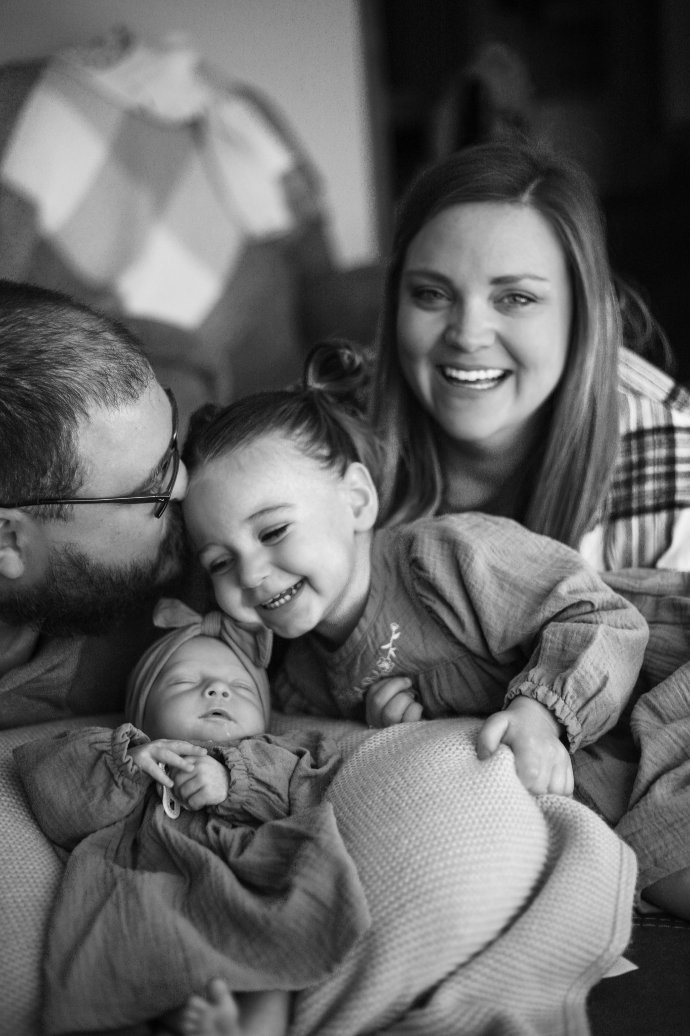 Family with two children, smiling and cuddling on a couch, in a cozy home setting.
