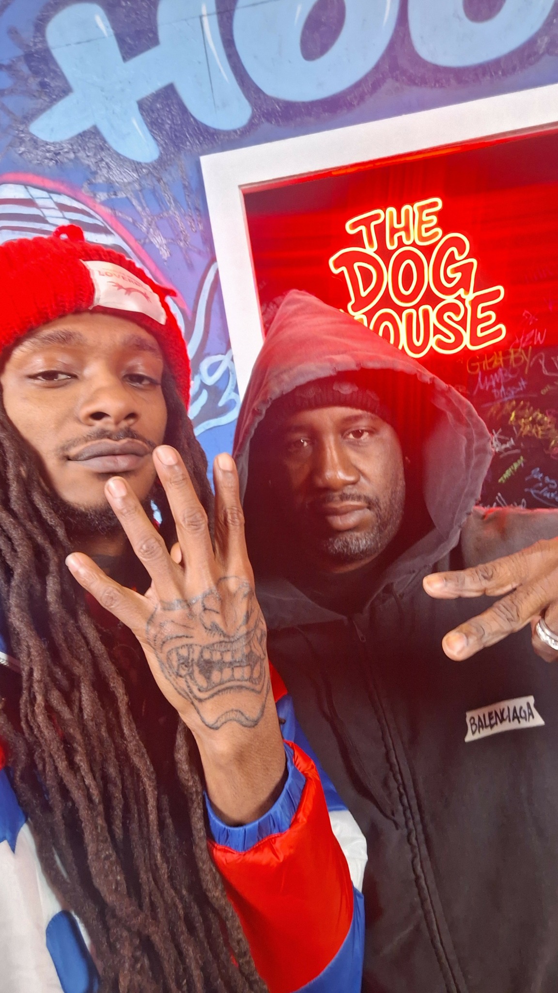 Two people posing with peace signs in front of a red sign that says 'The DUE'.