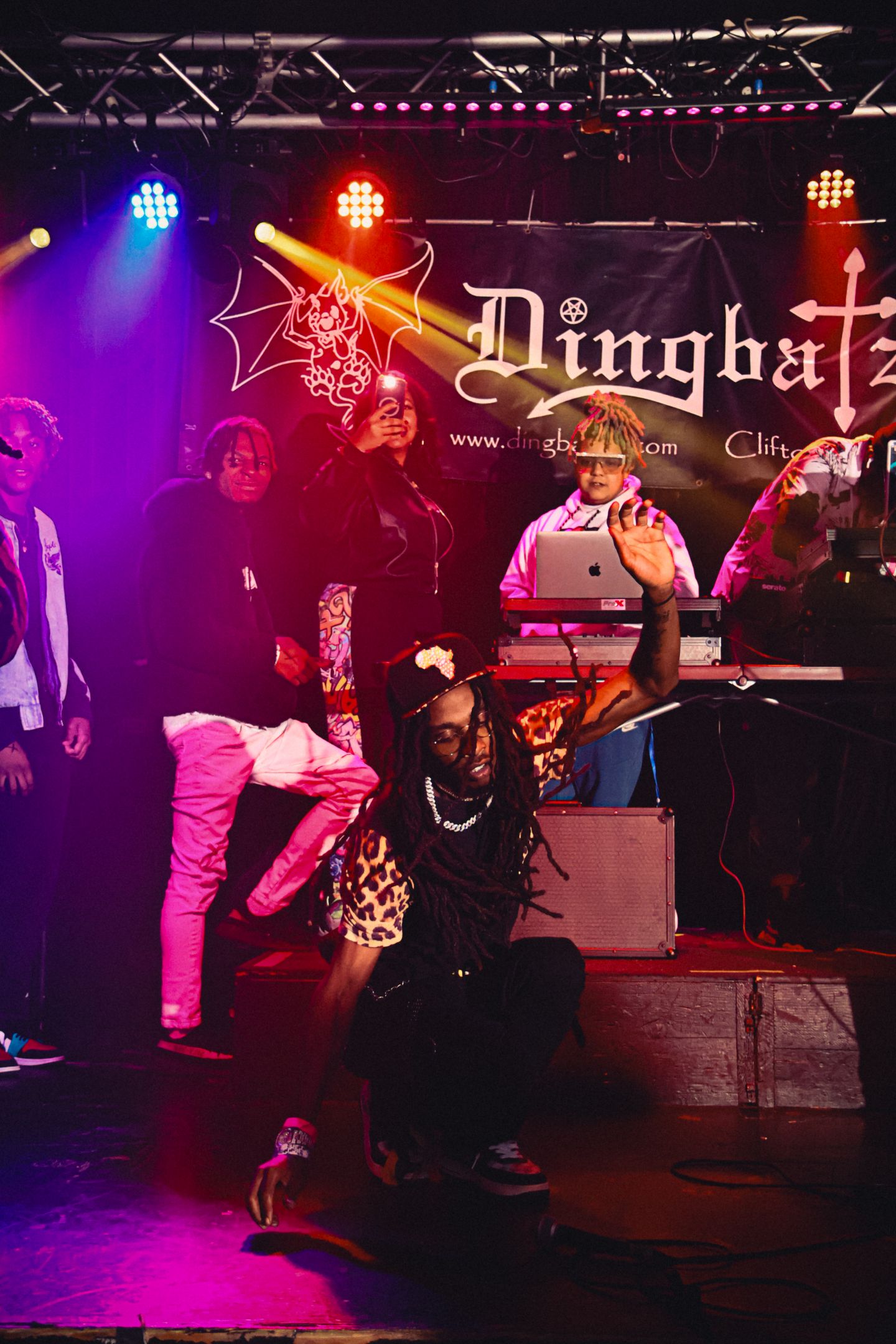 Group of people on stage with colorful lights, a banner, and musical instruments, celebrating or performing.