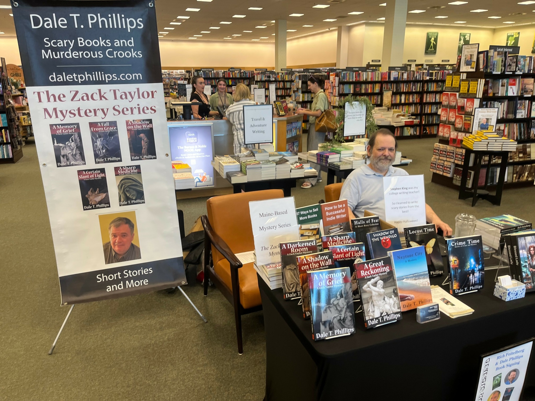 Book signing event at a bookstore with a man sitting behind a table displaying books and promotional signs.