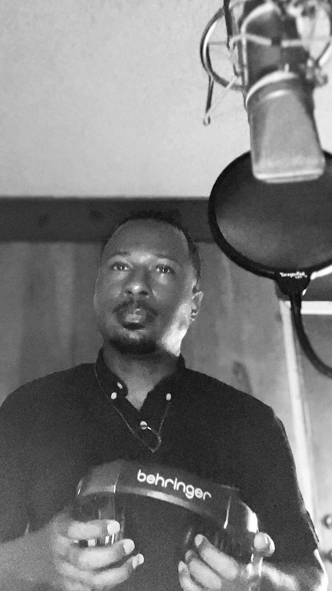 Person in a recording studio holding headphones, with a microphone and pop filter visible.