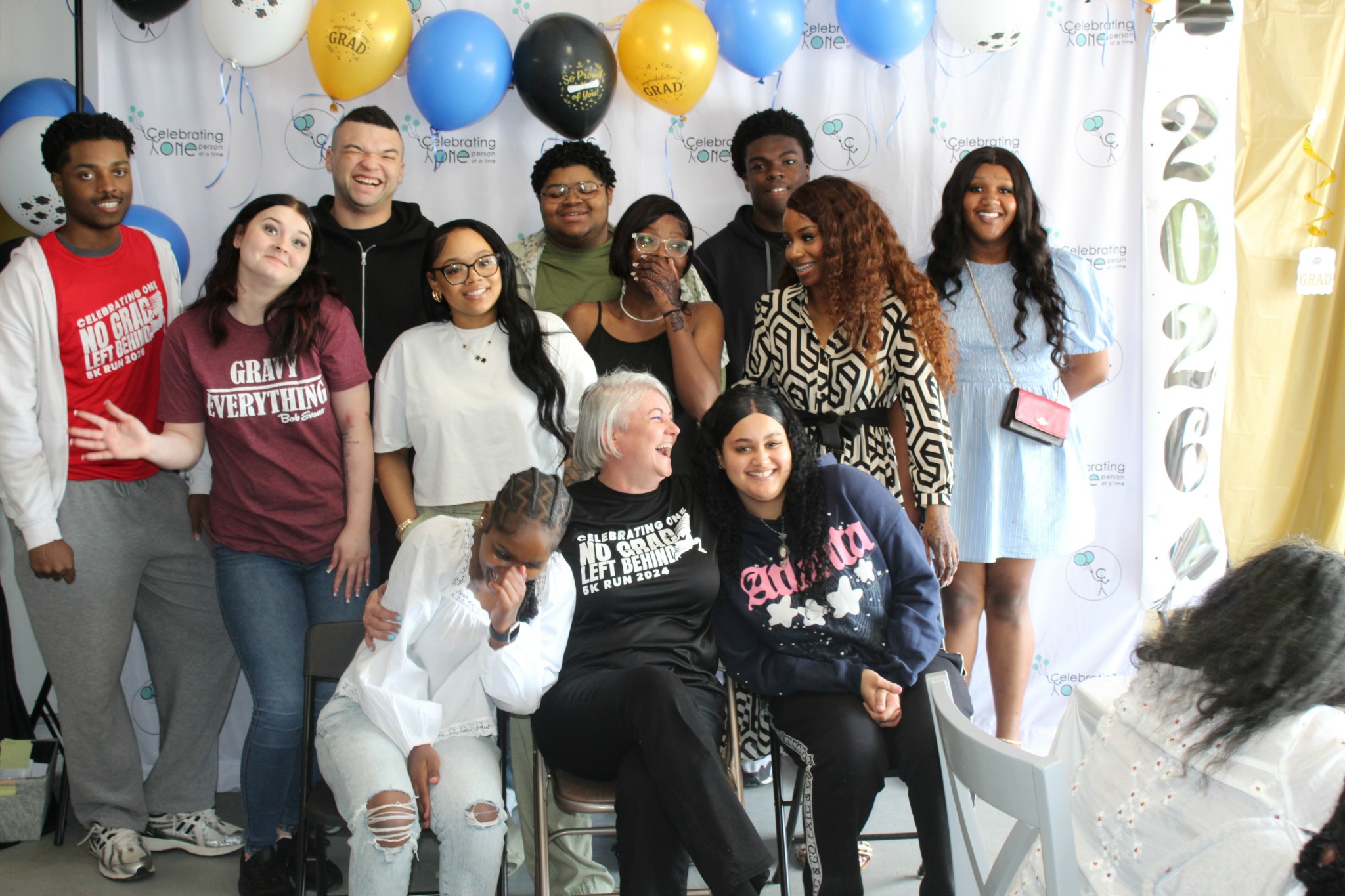 Group of diverse people celebrating with balloons and decorations, some smiling and posing for the photo.
