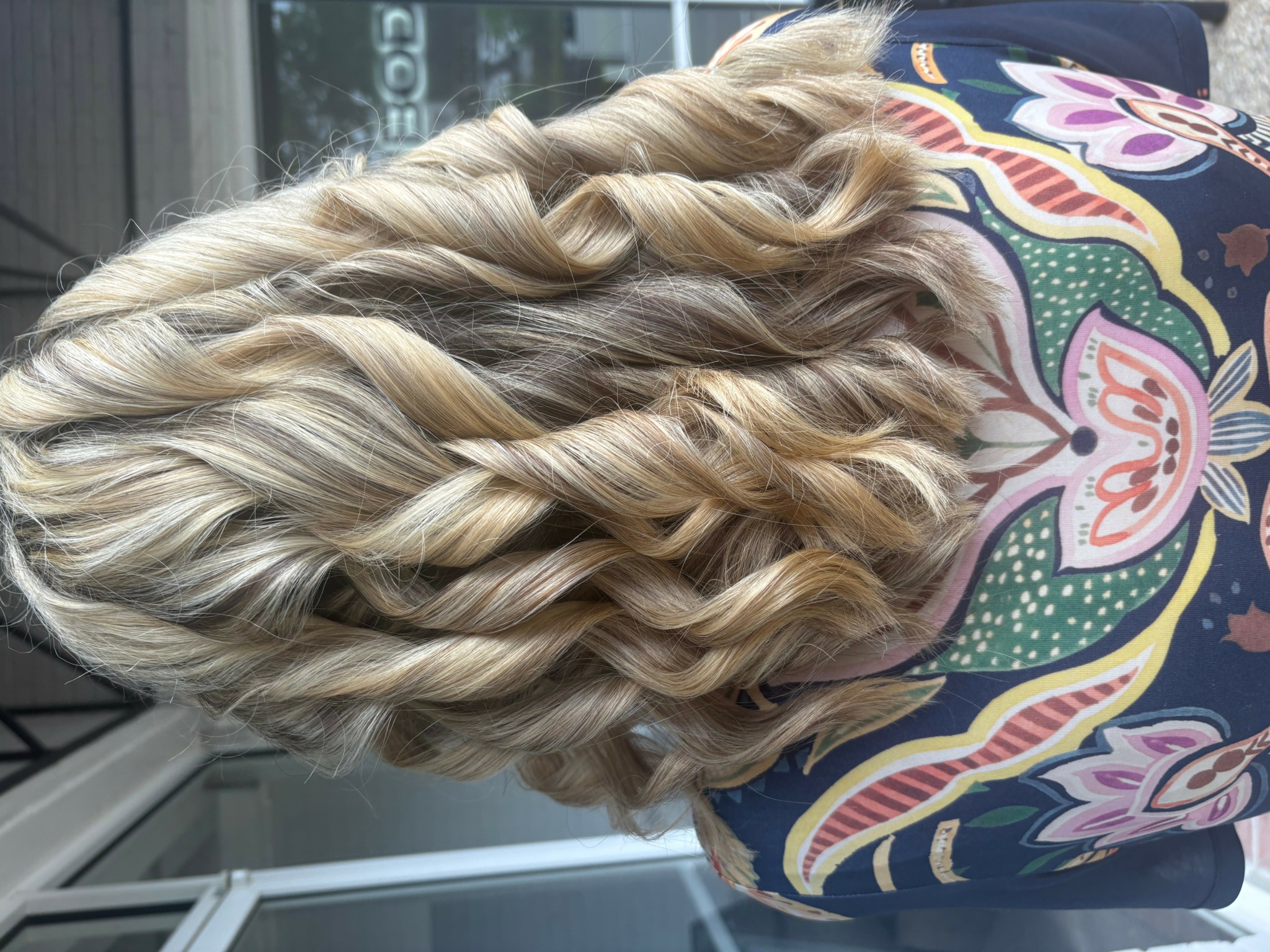 Person with long, blonde, curly hair seen from behind, wearing a colorful patterned top.