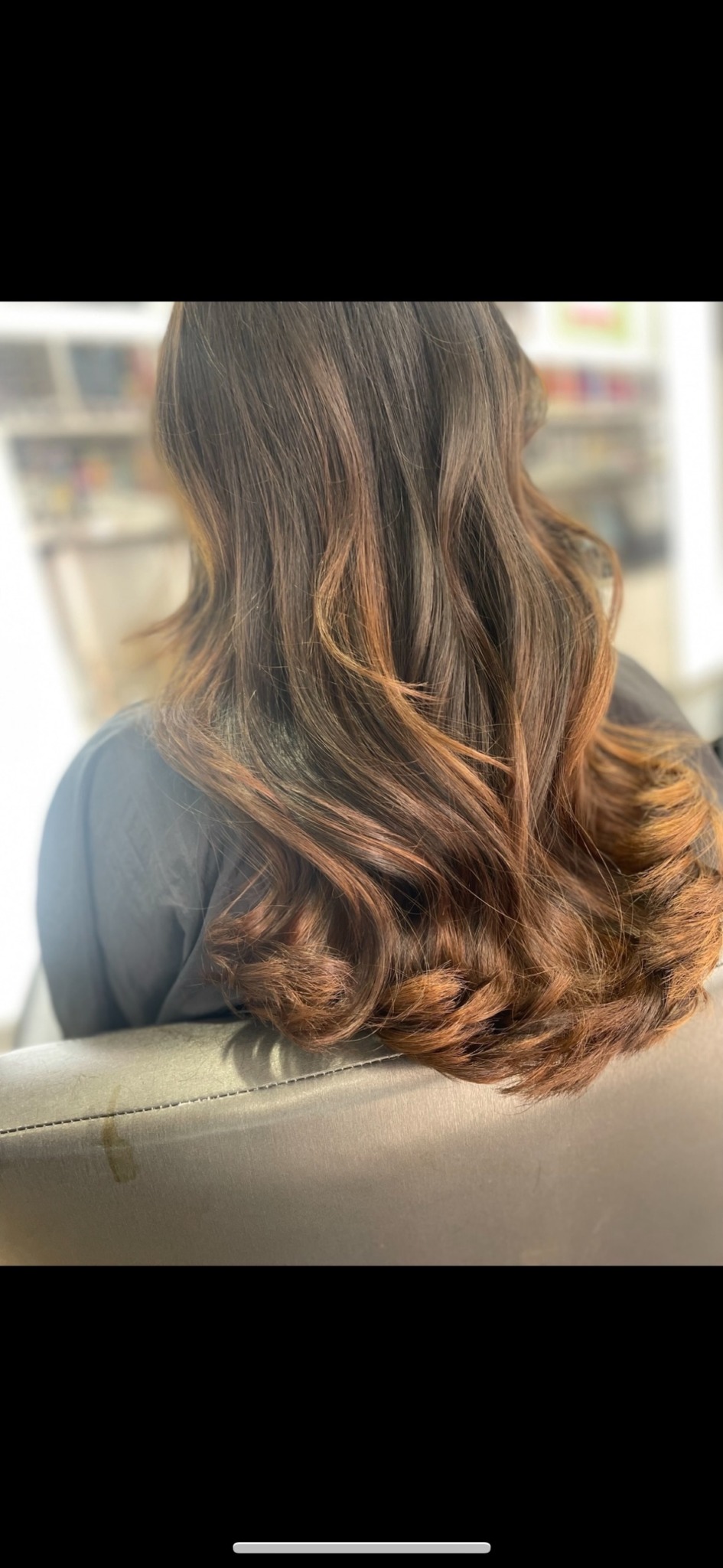 Back view of a person with long, wavy hair with brown highlights, sitting in a store or salon.