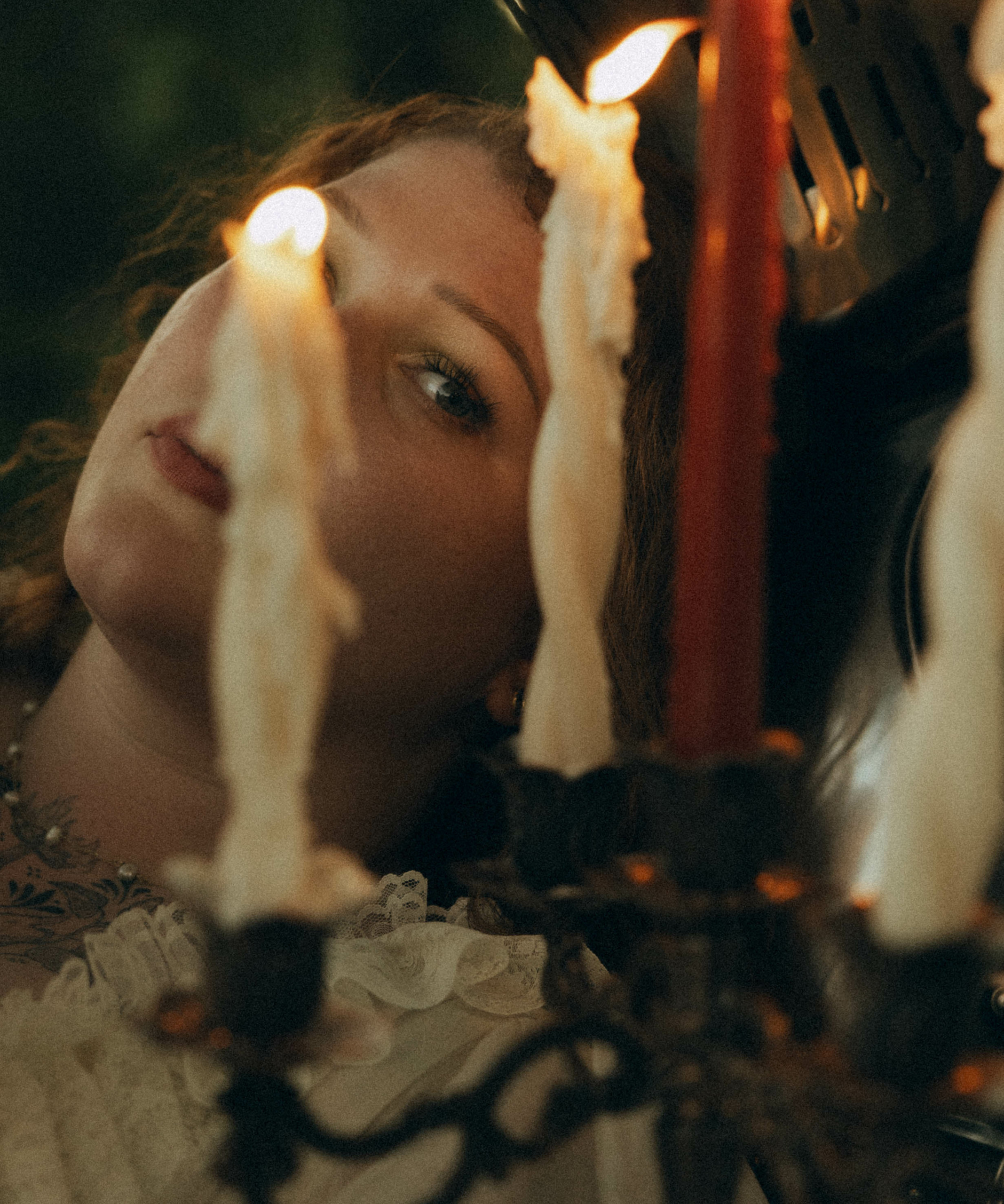 Person with face close to lit candles on a chandelier, focusing on the flames, with blurred background.
