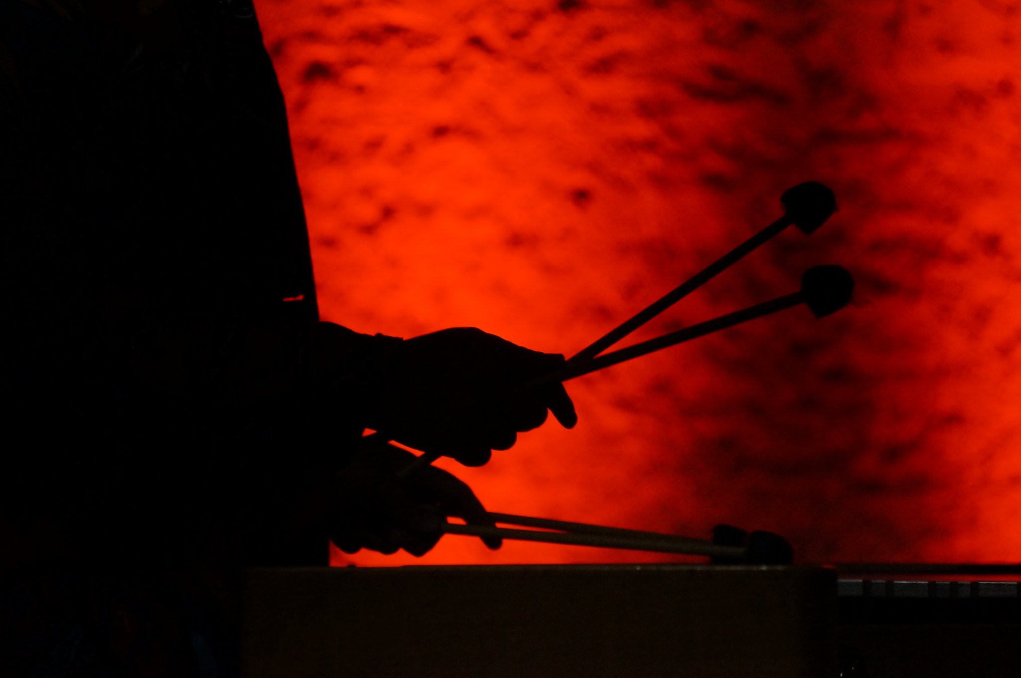 Silhouette of a person holding drumsticks against a red textured background.