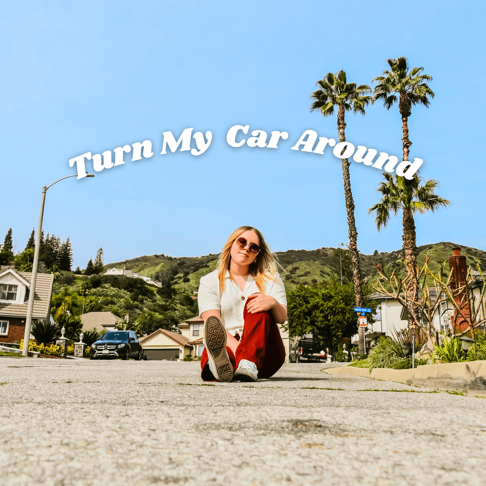 Young woman sitting on the street with palm trees and houses in background, blue sky, and text above reading 