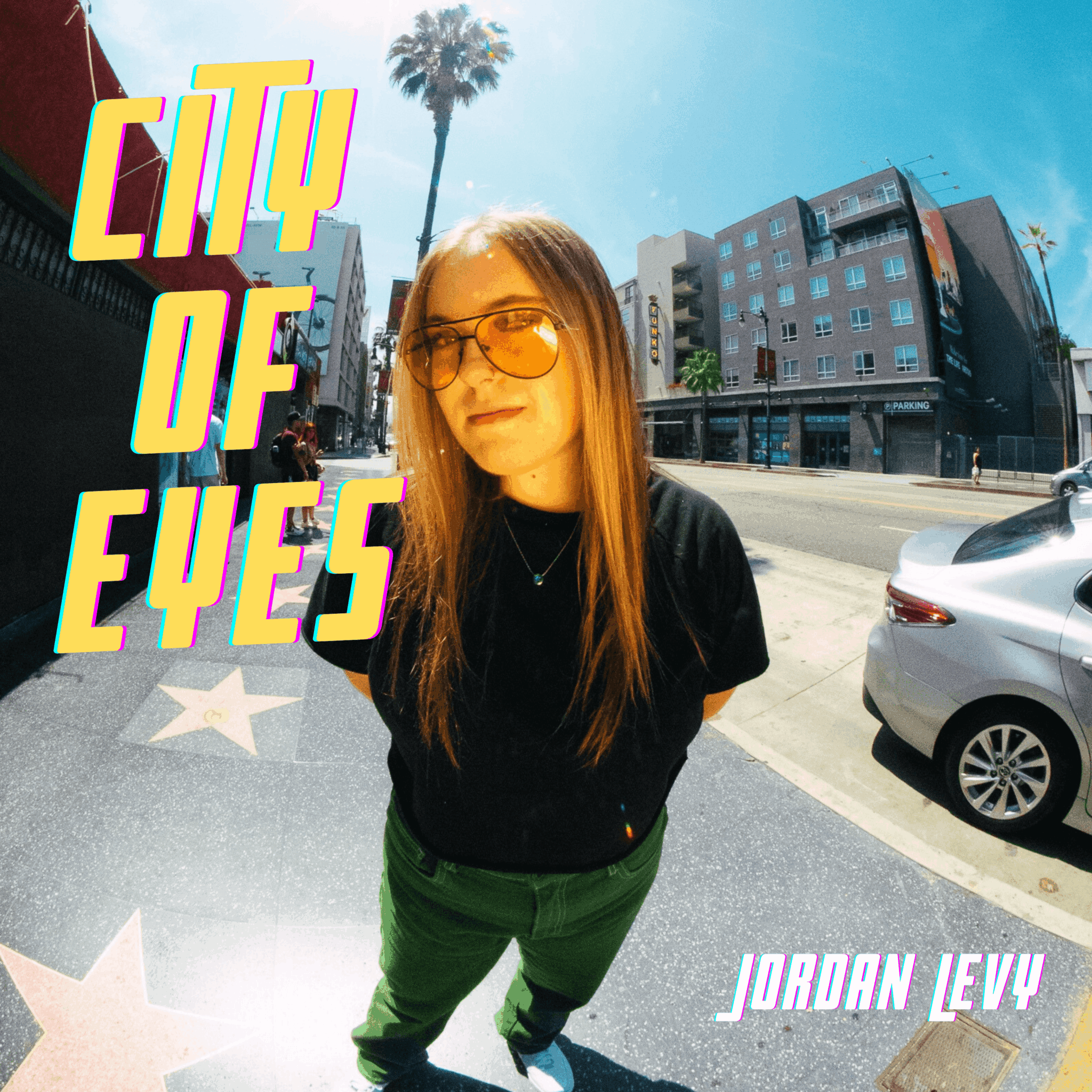 Young woman with long hair and sunglasses standing on city street with buildings and cars, sunny day.