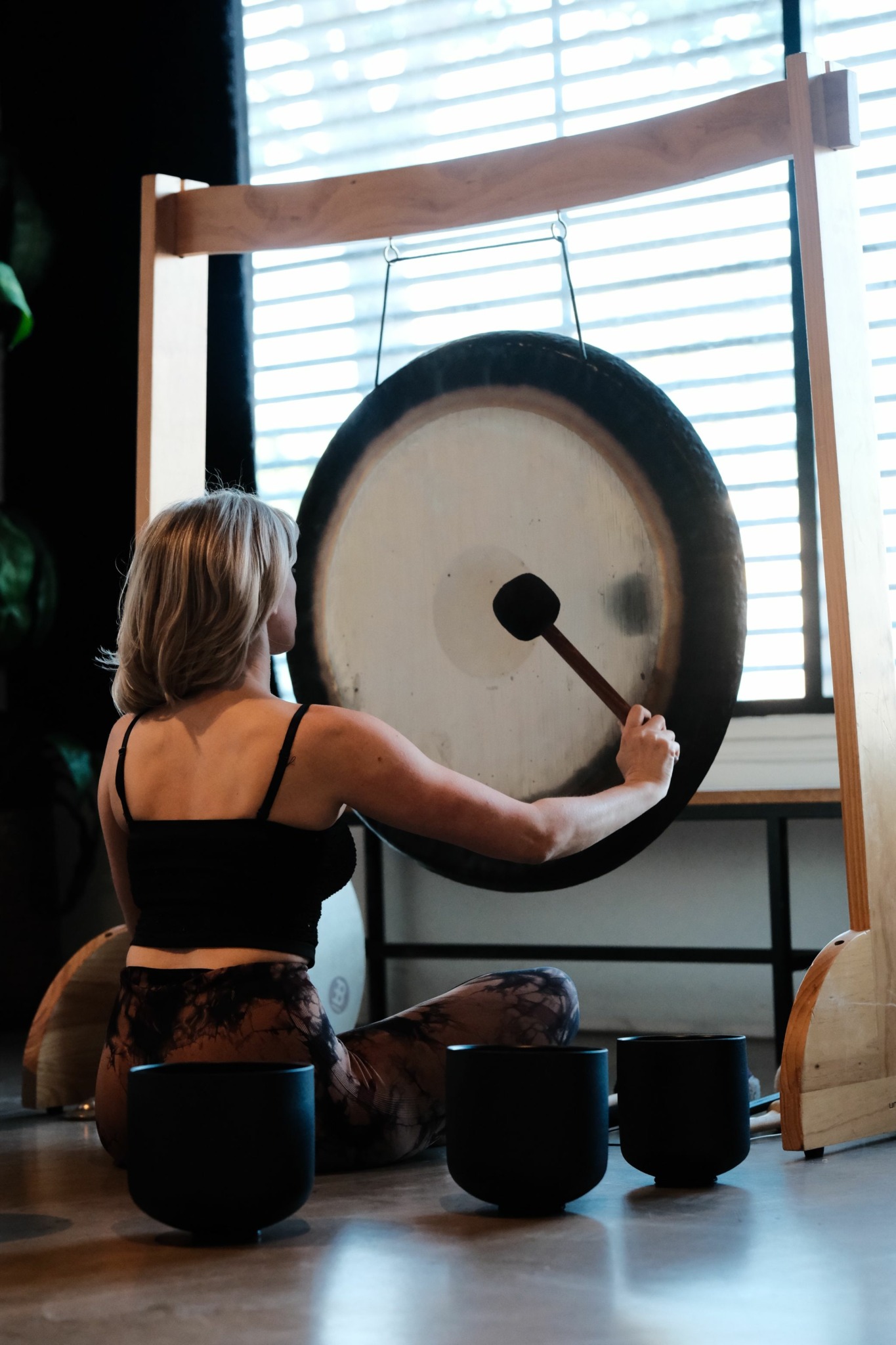 Person hitting a gong with a mallet in a room with large windows and natural light.