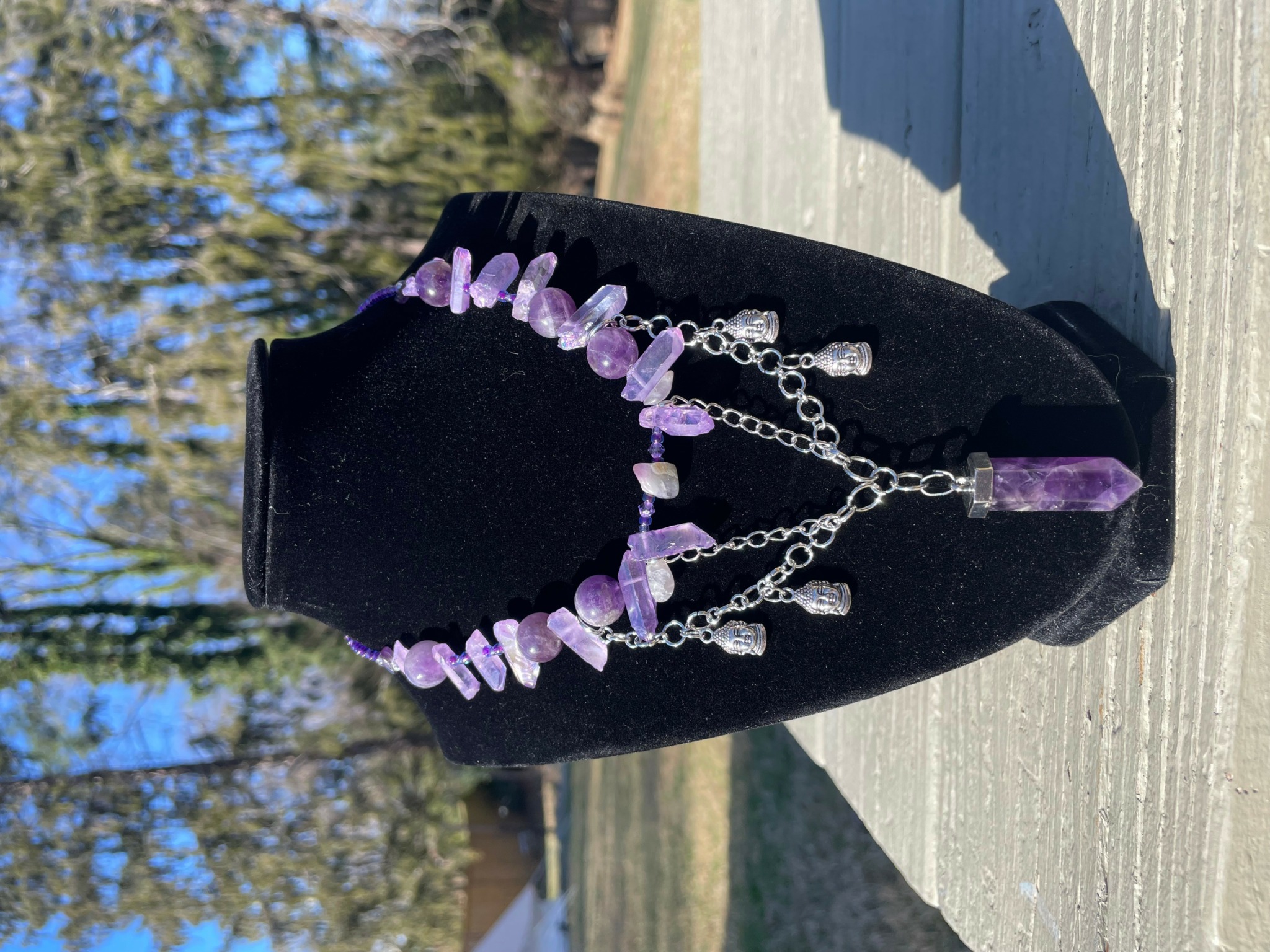 Purple gemstone necklace with chain and pendant displayed on a black bust outdoors.