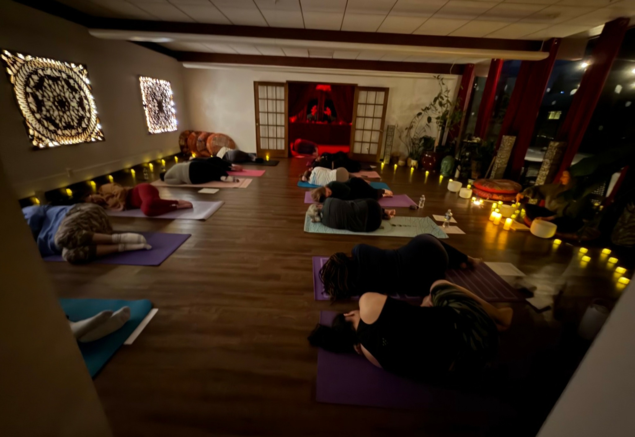 People practicing yoga on mats in a dimly lit room with decorative wall art and ambient lighting.