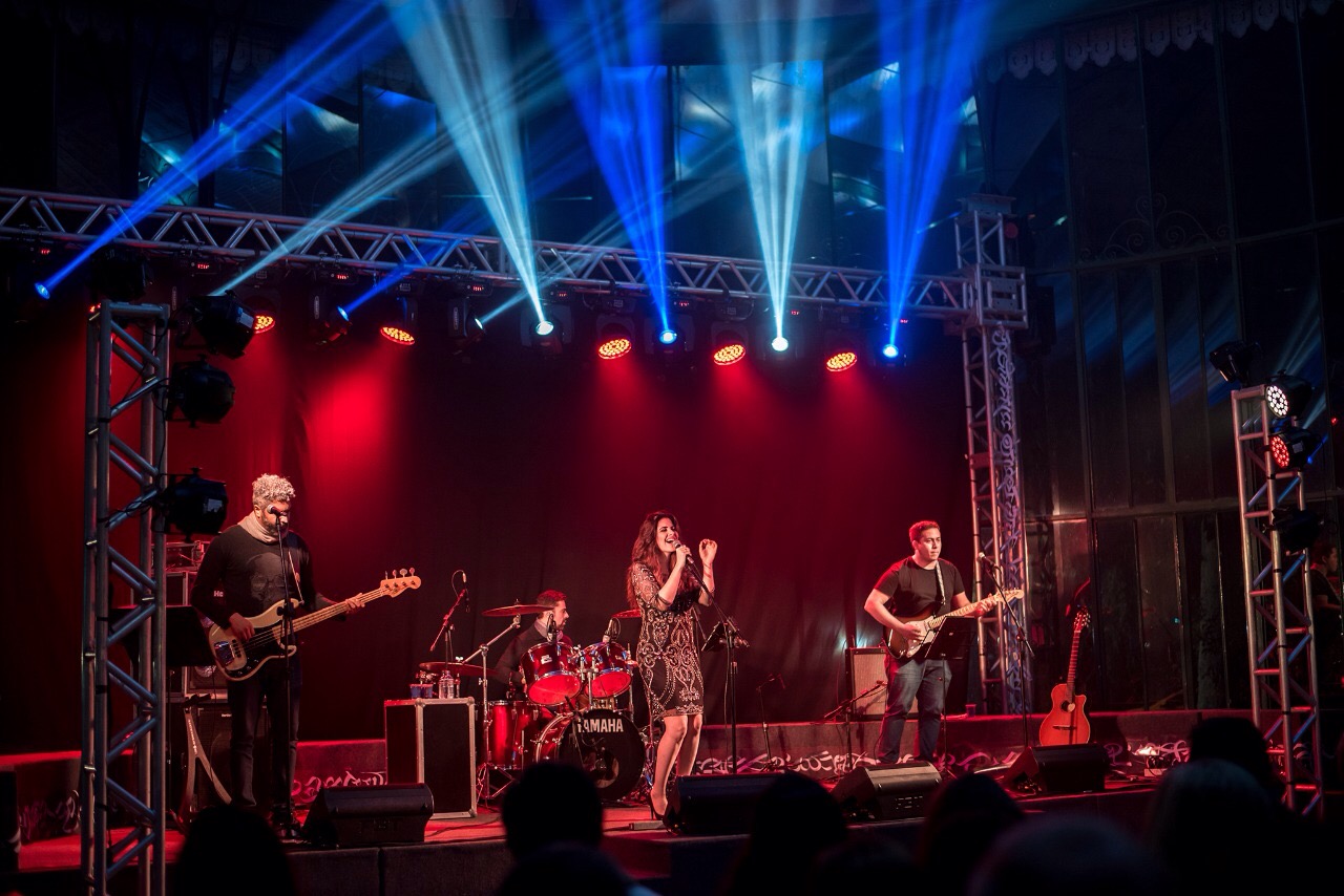 Band performs on stage with colorful lighting and audience in foreground.
