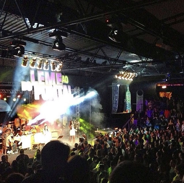 Concert stage with performers, bright lights, and an audience in a dark indoor venue.