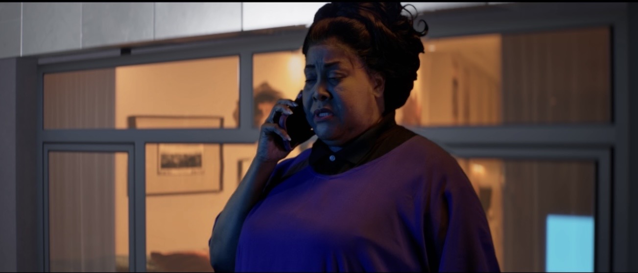 Woman talking on phone at night, illuminated by blue and warm lighting, standing near a window or glass door.