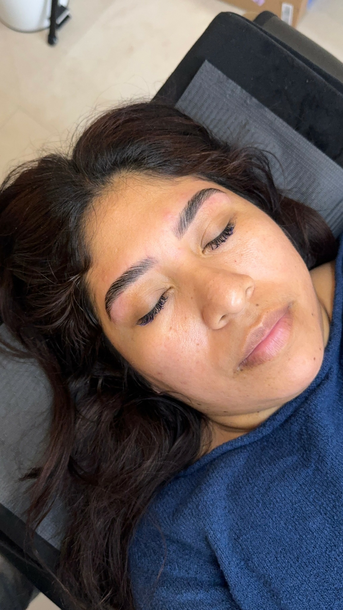 Young woman with closed eyes lying on a pillow, dark hair, and wearing a blue shirt.