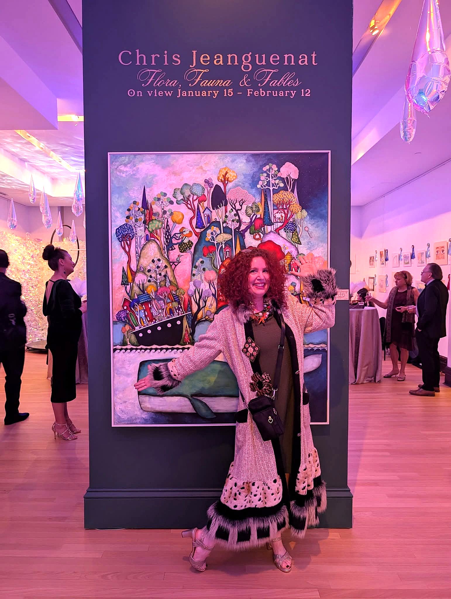 Woman with curly hair in front of colorful artwork at an art exhibition, surrounded by people in a gallery space.
