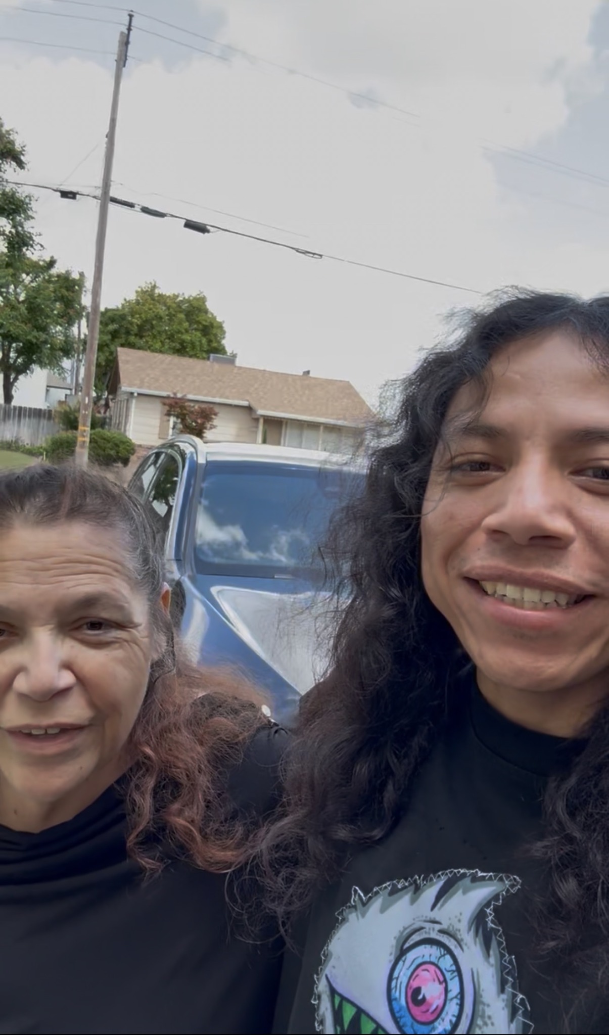 Two women taking a selfie outdoors with a car and trees in the background.