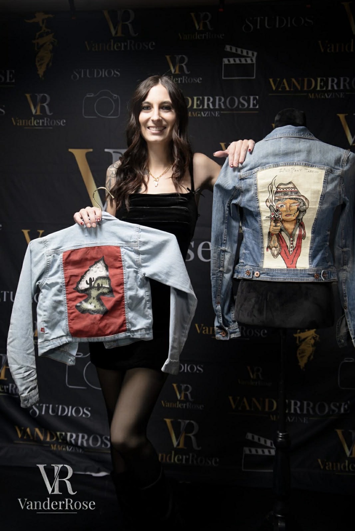 Woman with long dark hair holding two denim jackets with embroidered patches, smiling, black background with logos.