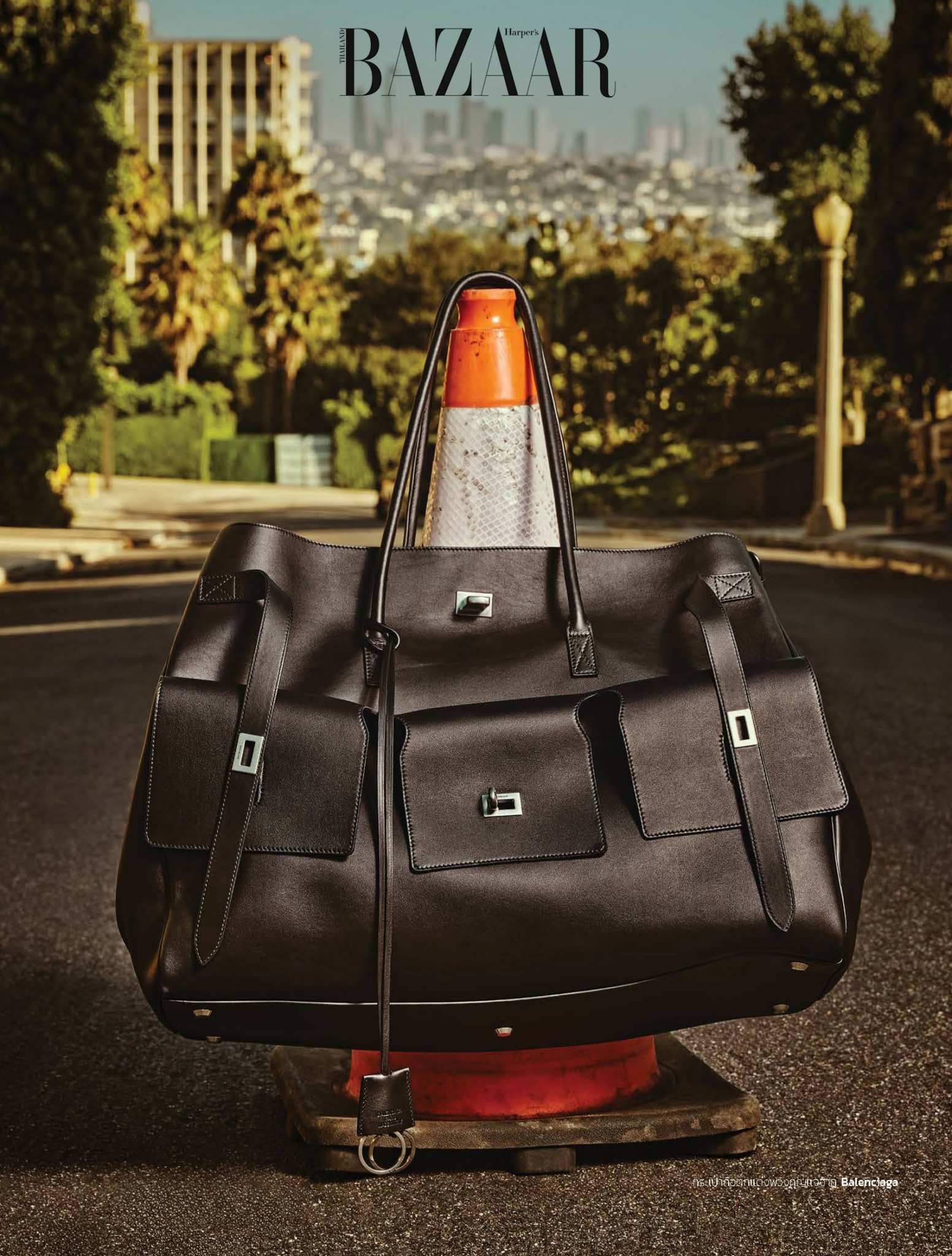 Black bag with orange traffic cone on top, on a city street with trees and buildings in background.