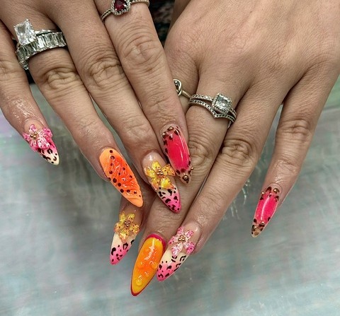 Two hands with colorful, decorated nails and rings, resting on a surface. Nails feature floral, animal, and abstract designs.