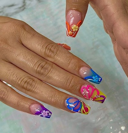 Hand with colorful floral and butterfly nail art, fingers resting on a surface, with a background of water or glass.