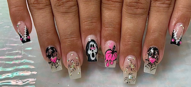 Nail art with Halloween-themed designs including ghosts, spiders, and spider webs, in black, pink, and white colors.