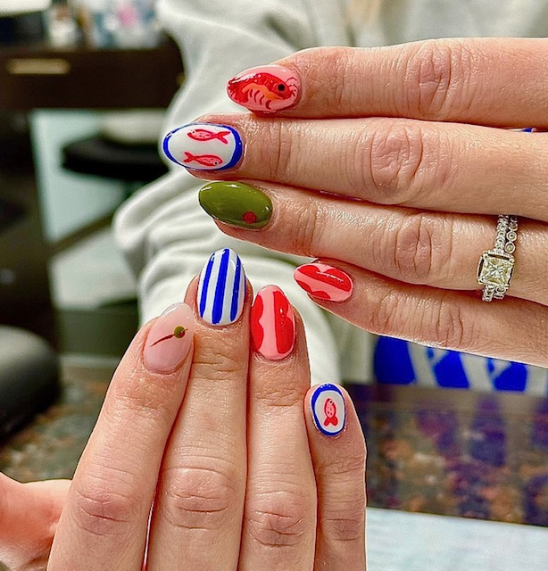 Close-up of hands with colorful, decorated nails, including red, blue, green, and pink designs, and a ring with a large stone.